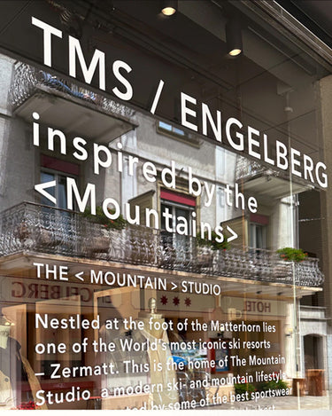 Person wearing the Z-4 L shell jacket in white from The Mountain Studio, featuring a minimalist design, adjustable hood, and water-resistant zippers, styled over an olive green midlayer in an outdoor setting.