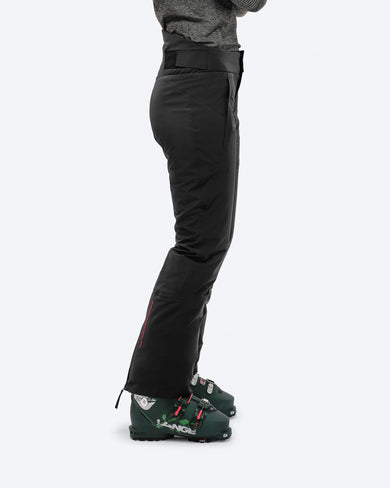 Woman wearing The Mountain Studio P-5 W black insulated ski pants with ergonomic fit, reinforced lower legs, and ski boots, highlighting the pants’ technical design and winter sports functionality.