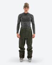 Model wearing The Mountain Studio Y-1 EPE green Gore-Tex ski pants with ergonomic pre-bent knees, large ventilation zippers, and reinforced scuff guards, paired with a technical baselayer and ski boots in a studio setting.