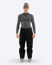 Man wearing The Mountain Studio Y-3 black shell ski pants with articulated knees and reinforced cuffs, paired with a technical long-sleeve top and ski boots, shown in a studio setting.
